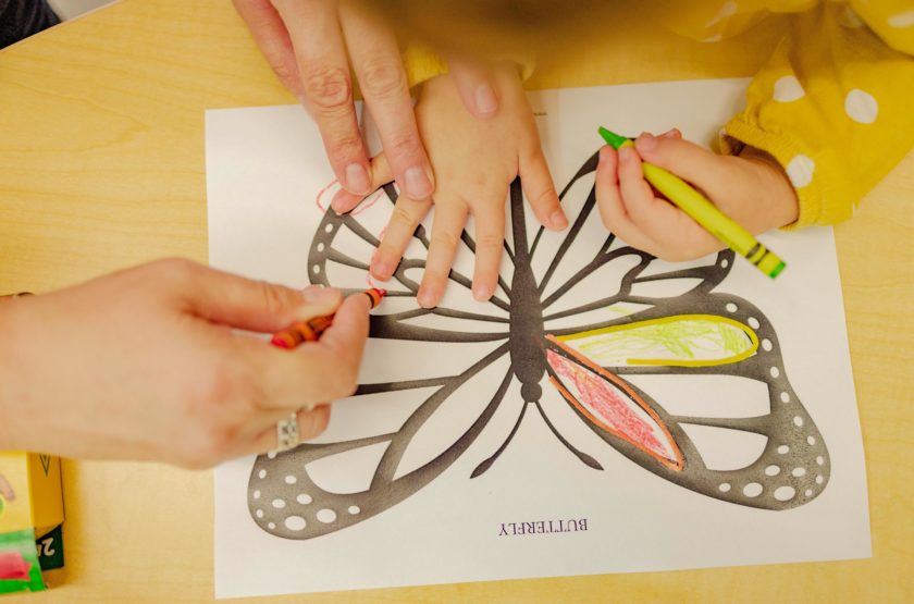 A child drawing a butterfly with a help of an adult.
