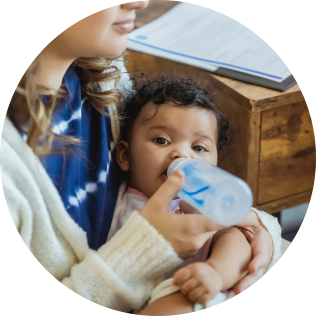 A woman is holding a baby and drinking from a bottle.