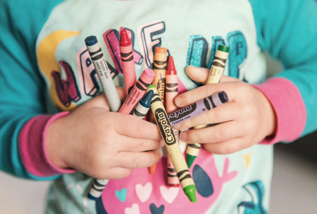 A toddler in a green shirt holding crayons.