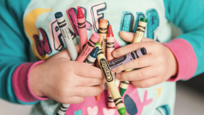 A toddler in a green shirt holding crayons.
