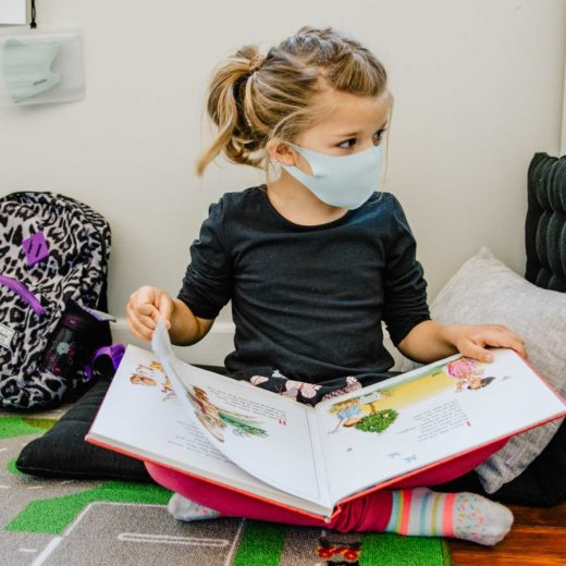A child wearing a mask reading a book.