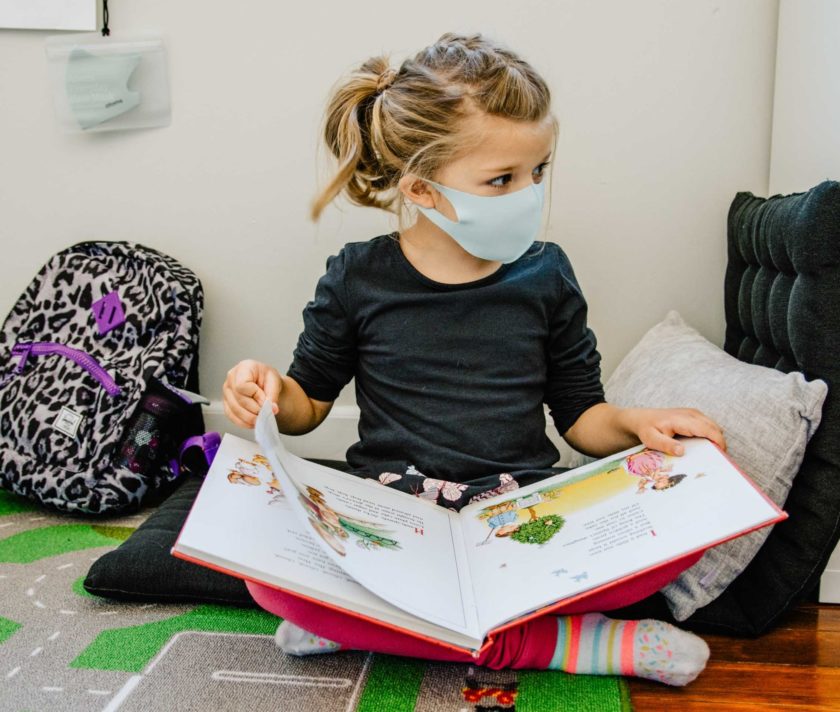 A child wearing a mask reading a book.