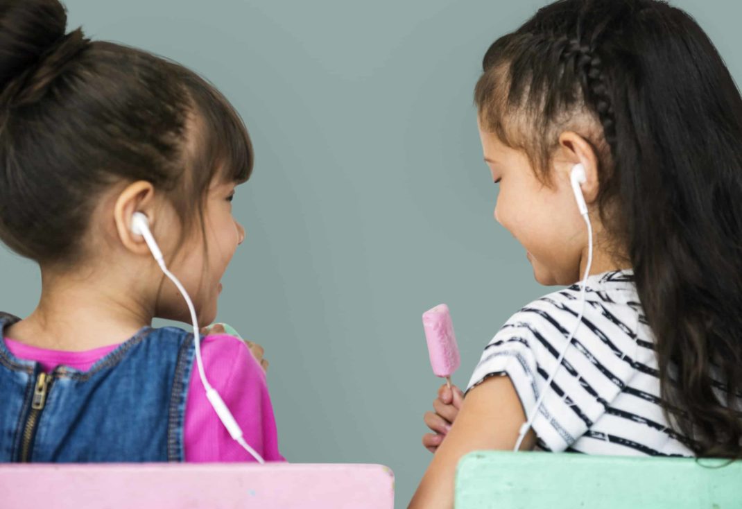 Two young girls sharing earbuds.