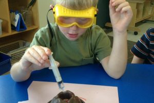 A boy wearing goggles and a lab coat is working on a project.