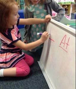 Two little girls writing on a white board.