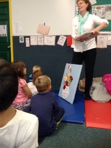 A woman reading a book to children in a classroom.