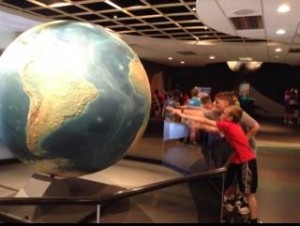 A group of kids looking at a large globe in a museum.