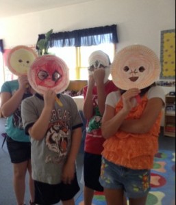 A group of children holding paper masks in a classroom.