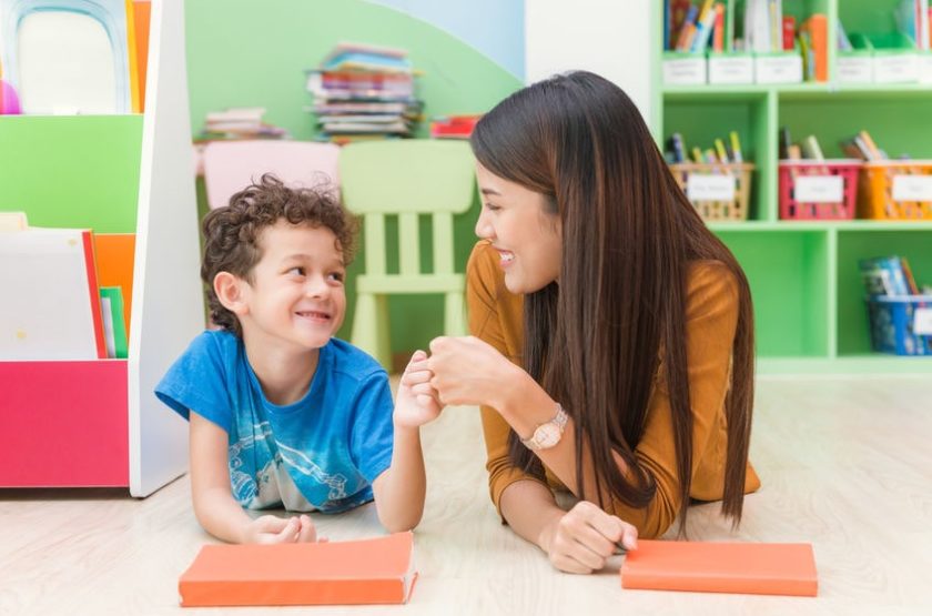 A woman and a boy are sitting on the floor in a classroom.