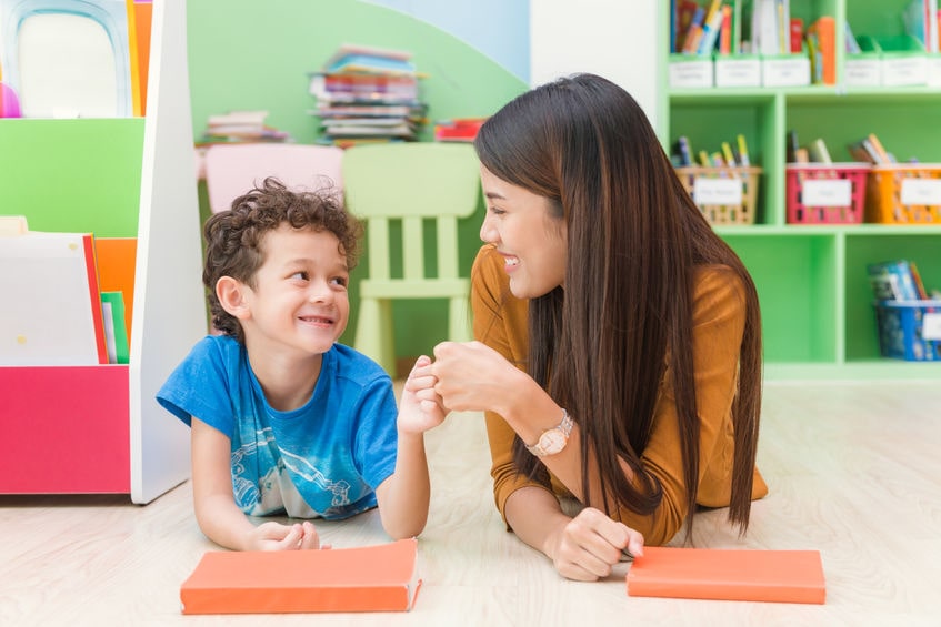 A woman and a boy are sitting on the floor in a classroom.