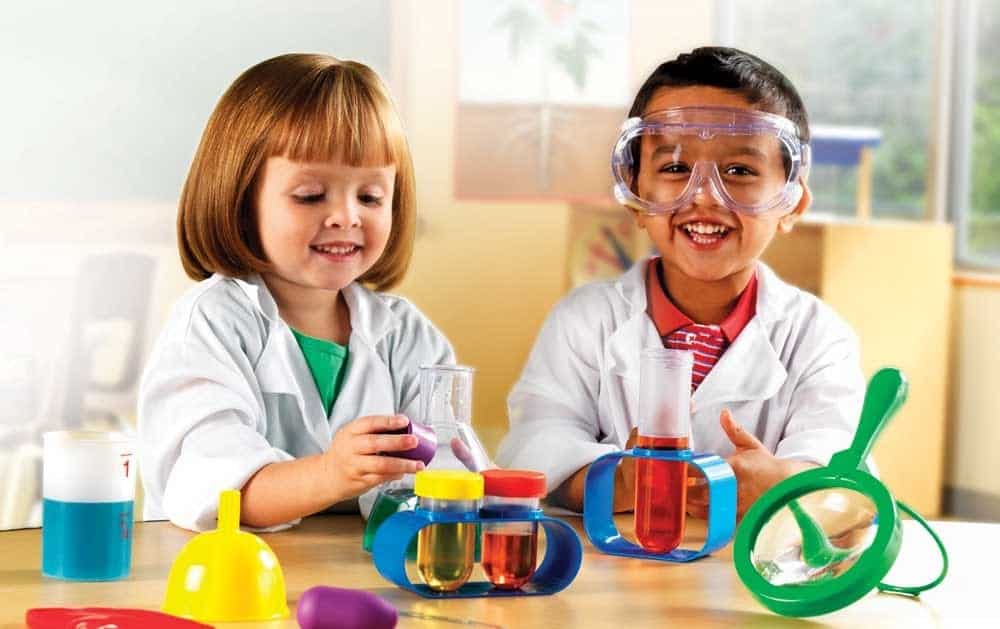 Two children in lab coats playing with toys.