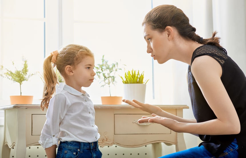 A woman is talking to a little girl in front of a window.