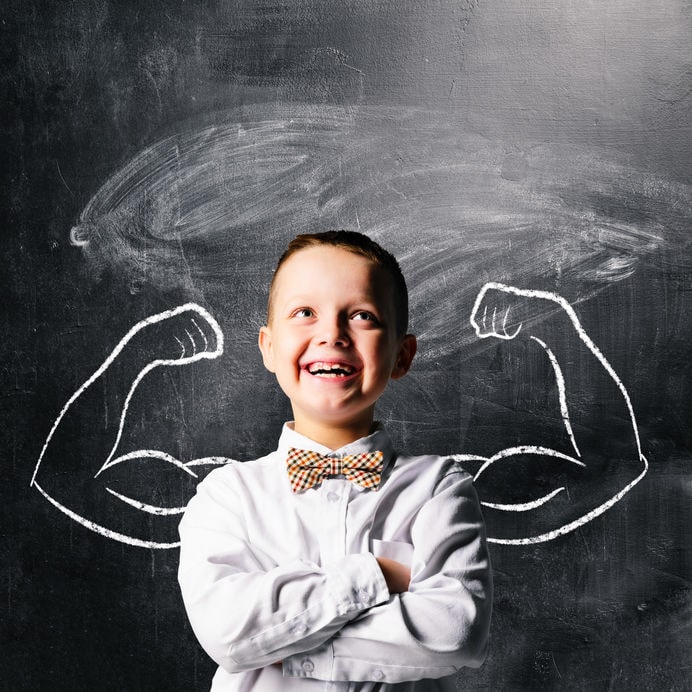 A young boy is standing in front of a chalkboard with a drawing of muscles.