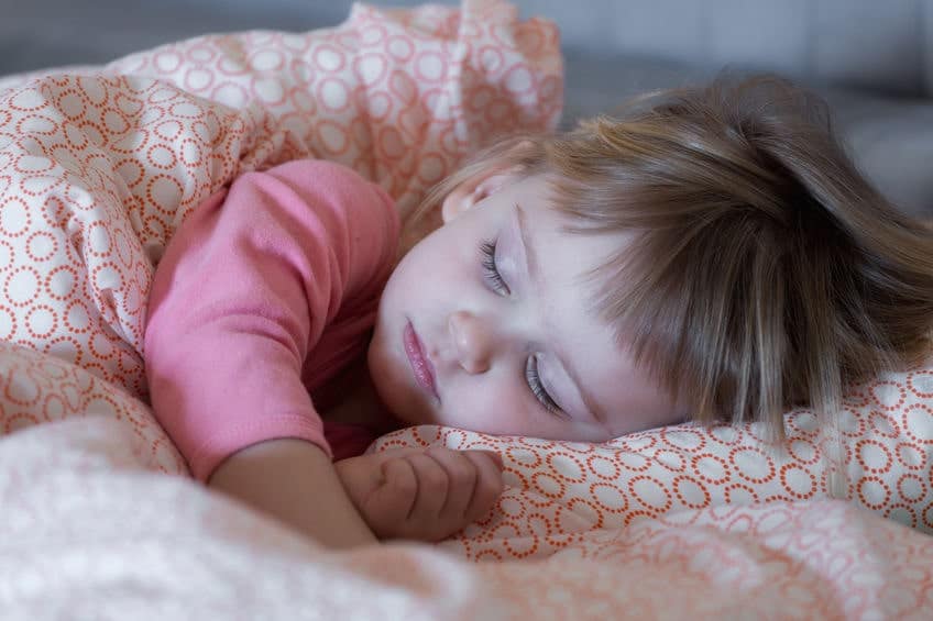 A little girl sleeping on a bed with a pink blanket.