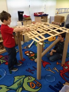 Two boys playing with a wooden table in a classroom.