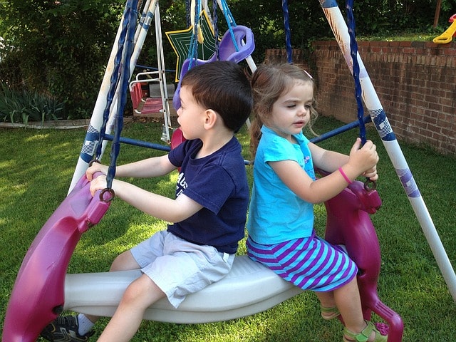 Two children sitting on a swing in a backyard.