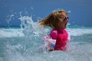 A little girl in a pink swimsuit splashing in the ocean.