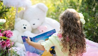 A little girl reading to her stuffed animals.