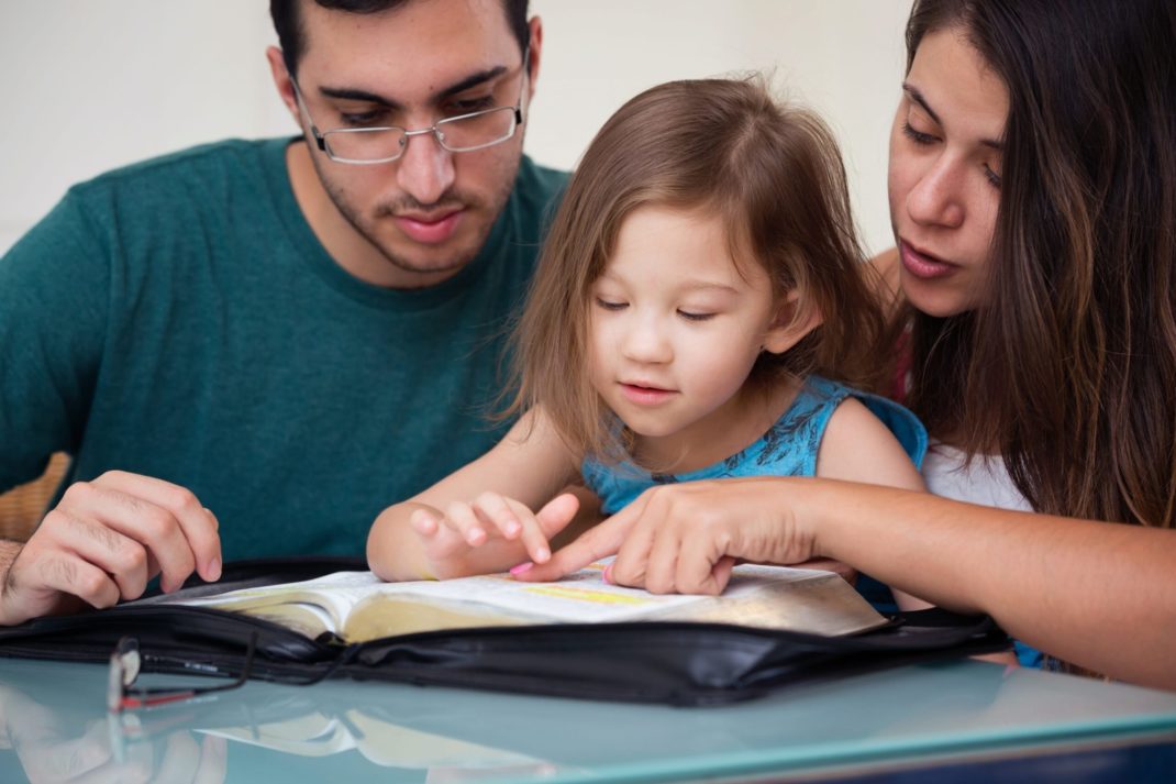 Two parents helping a young child with reading.