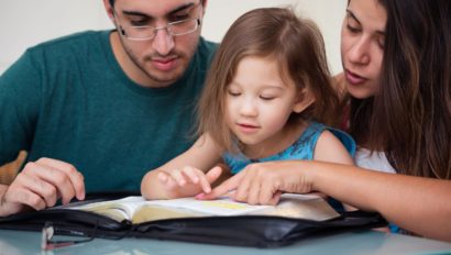 Two parents helping a young child with reading.