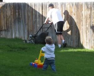 Dad mowing the lawn with toddler