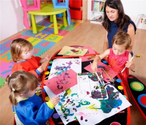 A group of children are painting at a table in a playroom.