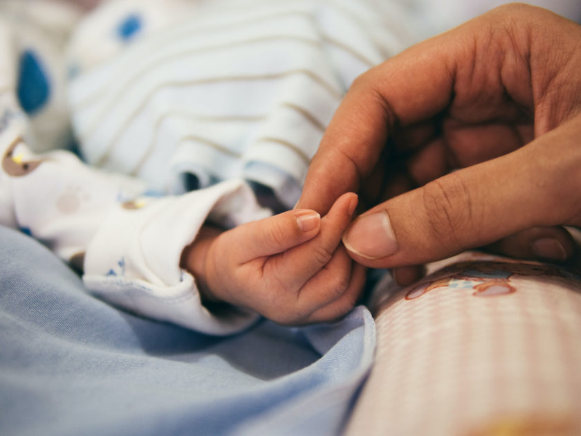 A caregiver holding the hand of an infant.
