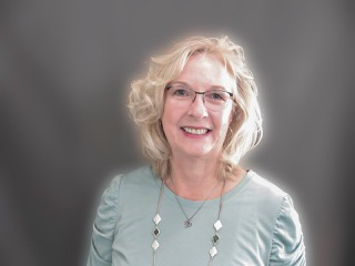 Mariann gladstone standing in front of a grey background.