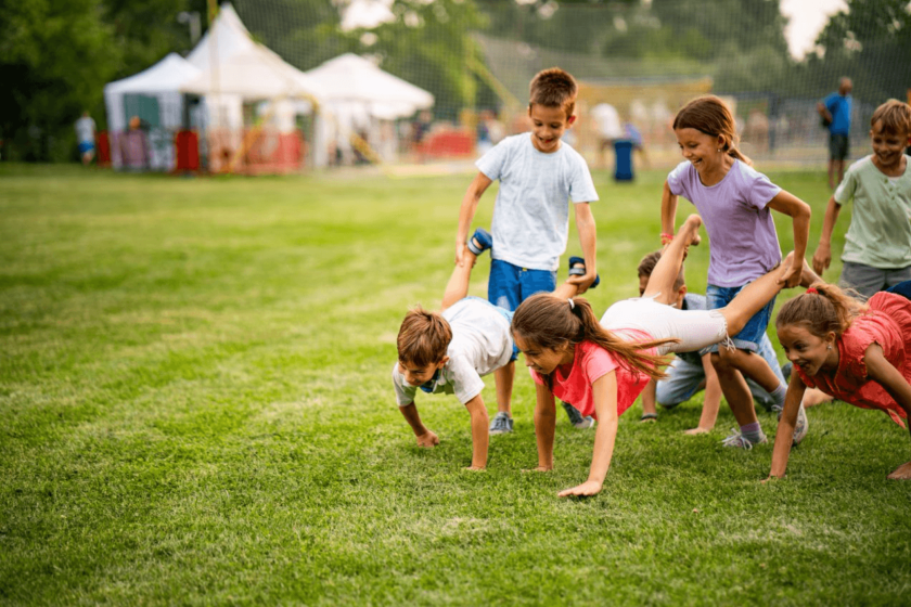 A group of children doing a wheelbarrow run on a grassy field.