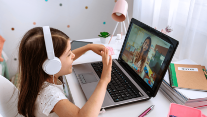 A girl wearing headphones sits at a desk, engaging in a video call on a laptop.