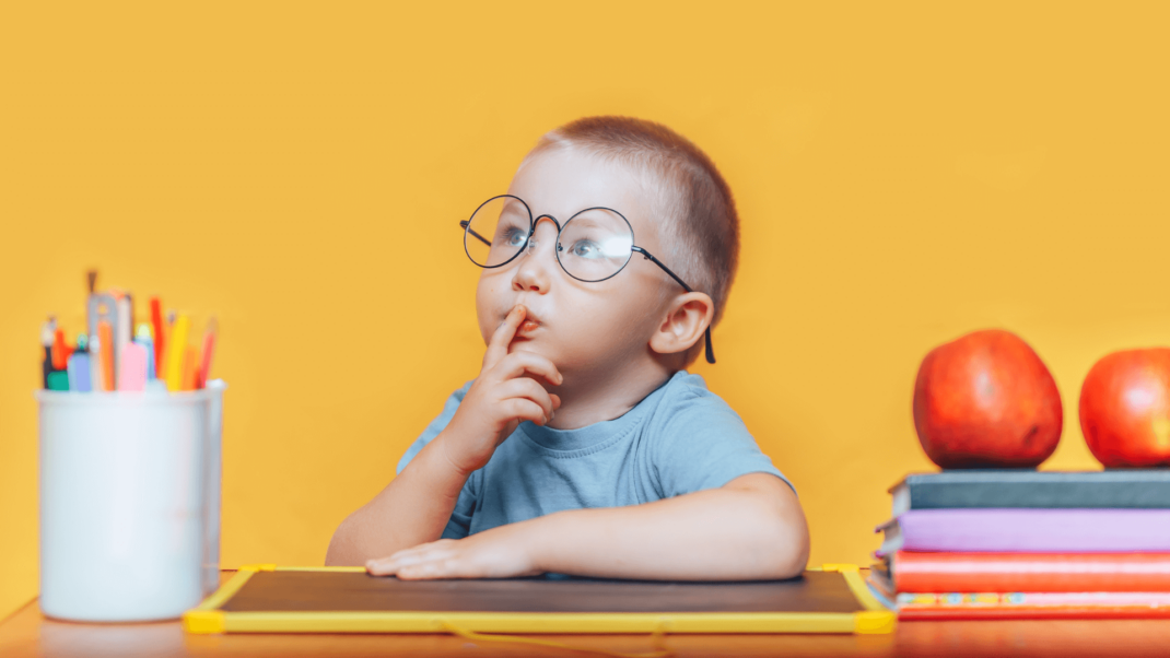 A child wearing glasses sits at a desk with a thoughtful expression, surrounded by colorful pencils, a chalkboard, two apples, and stacked books against an orange background.